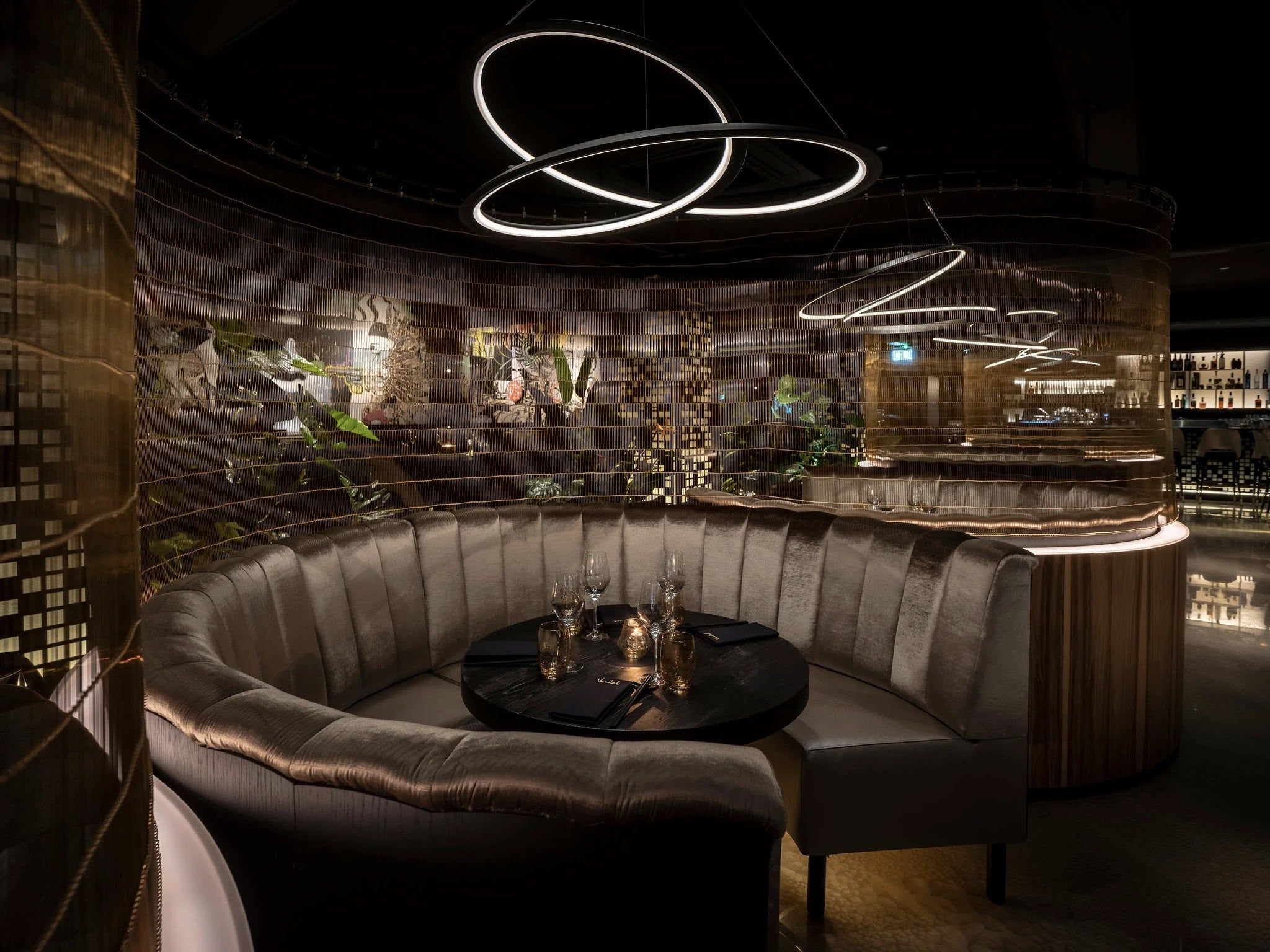 Ronde loungebank rond een tafel onder zwevende lichtringen in restaurant Vandal