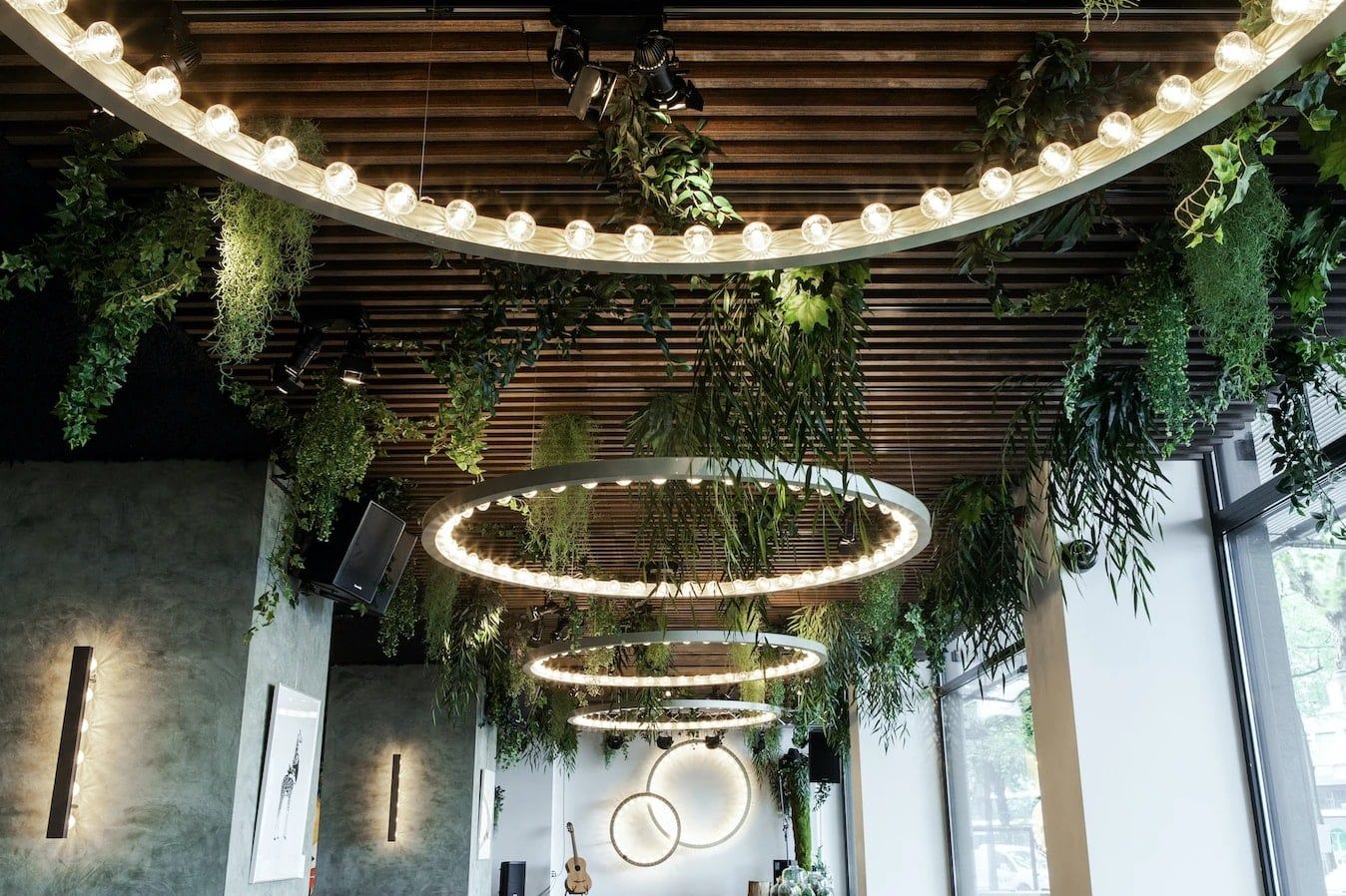 Grote ringvormige hanglampen met lichtbollen onder een houten lamellenplafond vol planten