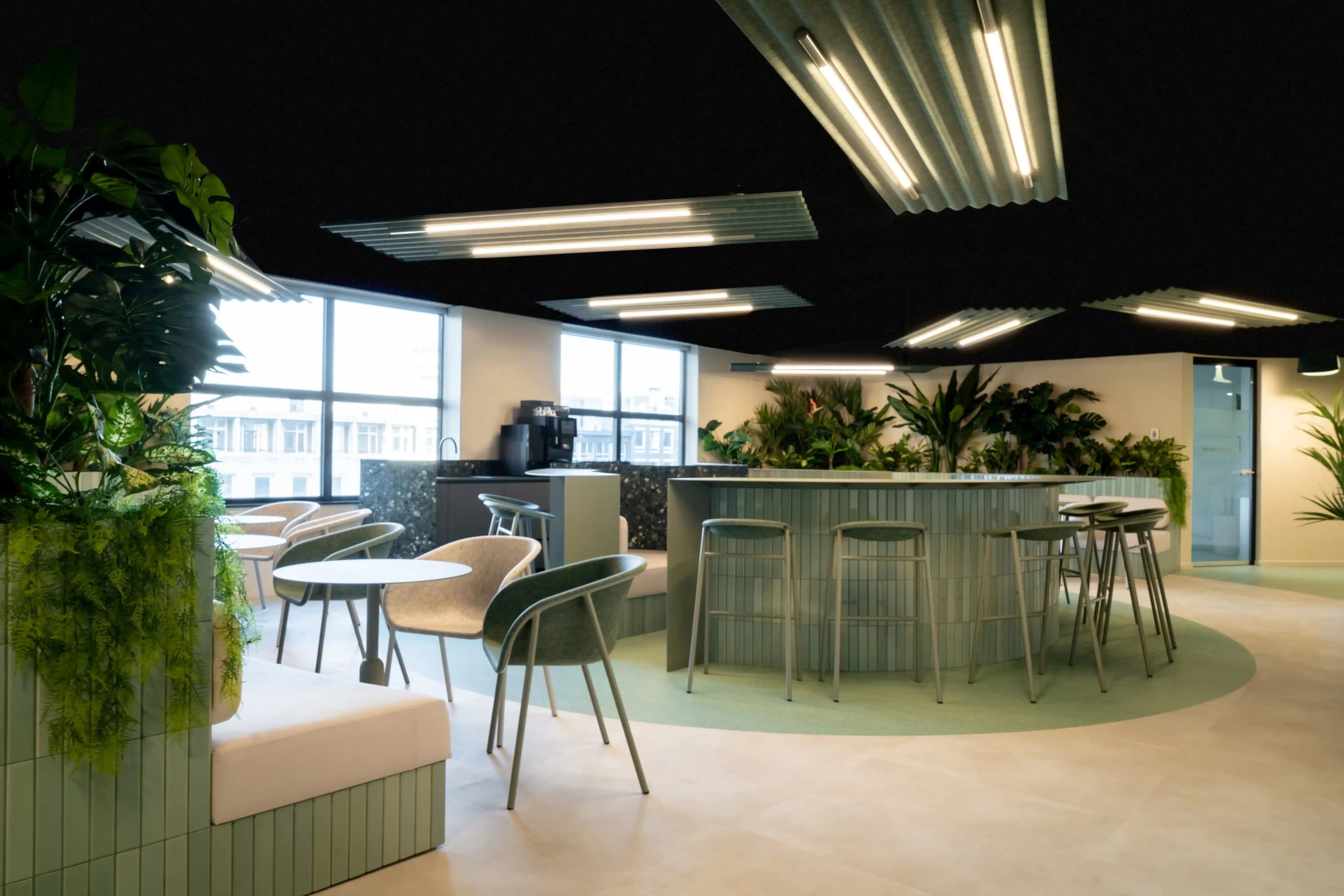 Lounge met ronde bar, groene zitbanken en planten onder lineaire armaturen in een zwart plafond