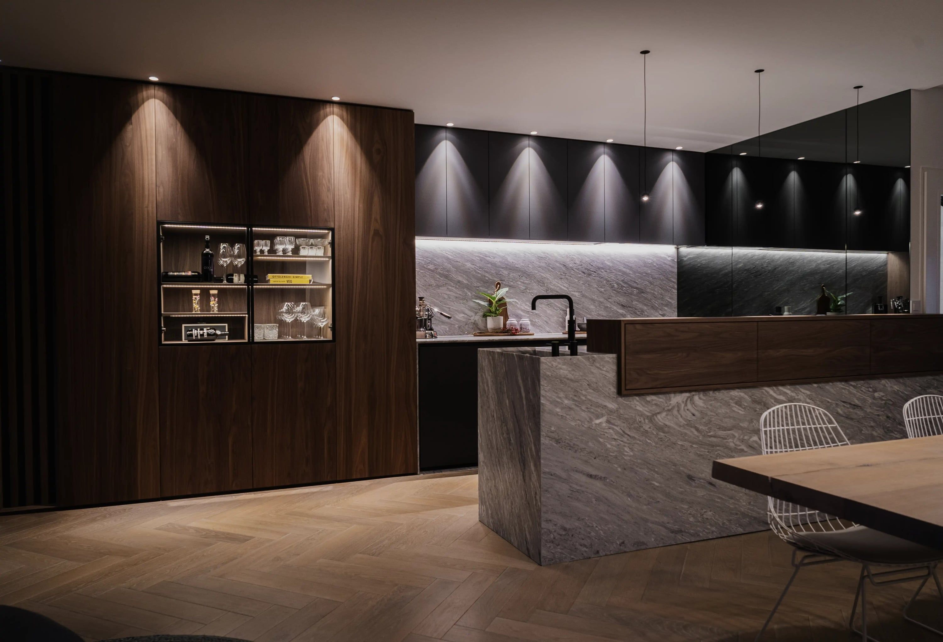 Keuken met notenhouten kastenwand, verlichte glazen vitrine en een marmeren kookeiland