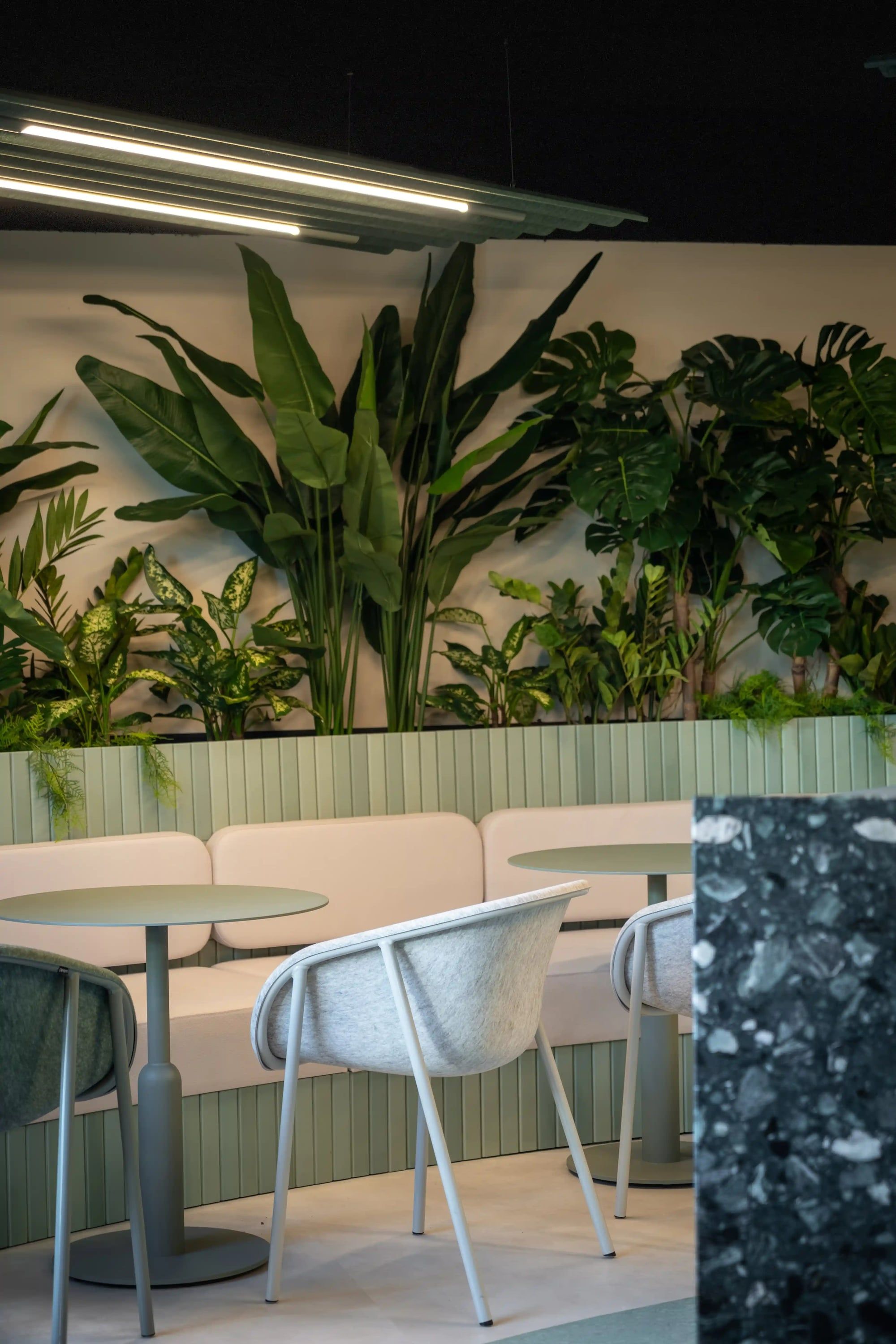 Zitbank met ronde tafels en grijze stoelen onder een wand vol tropische planten