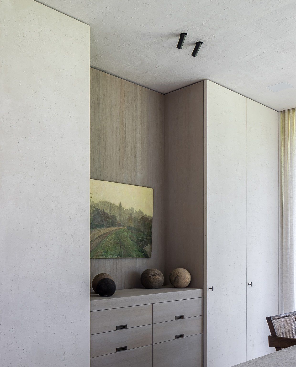 Twee zwarte opbouwspots in een betonnen plafond boven een kast met een schilderij en houten bollen