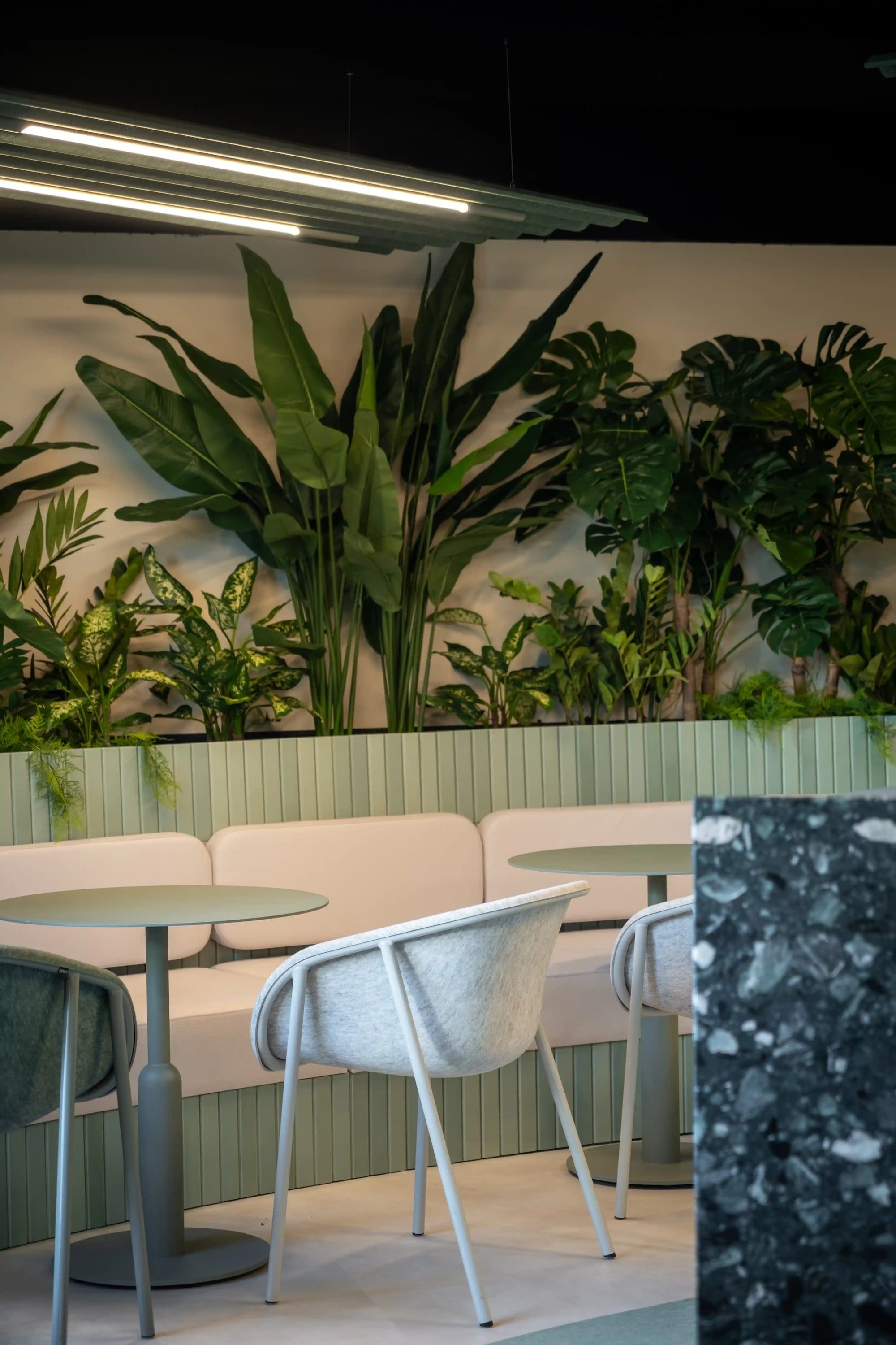 Zithoek met groene zitbank en grijze stoelen, met een terrazzo tafelblad op de voorgrond