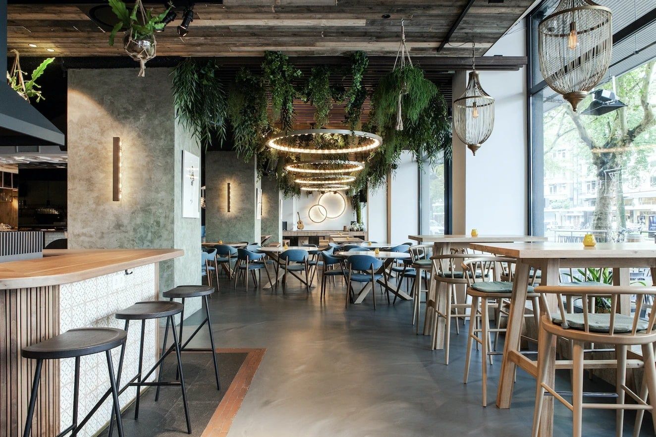 Restaurant met bar, houten krukken en tafels langs de pui, met ringlampen en wandarmaturen