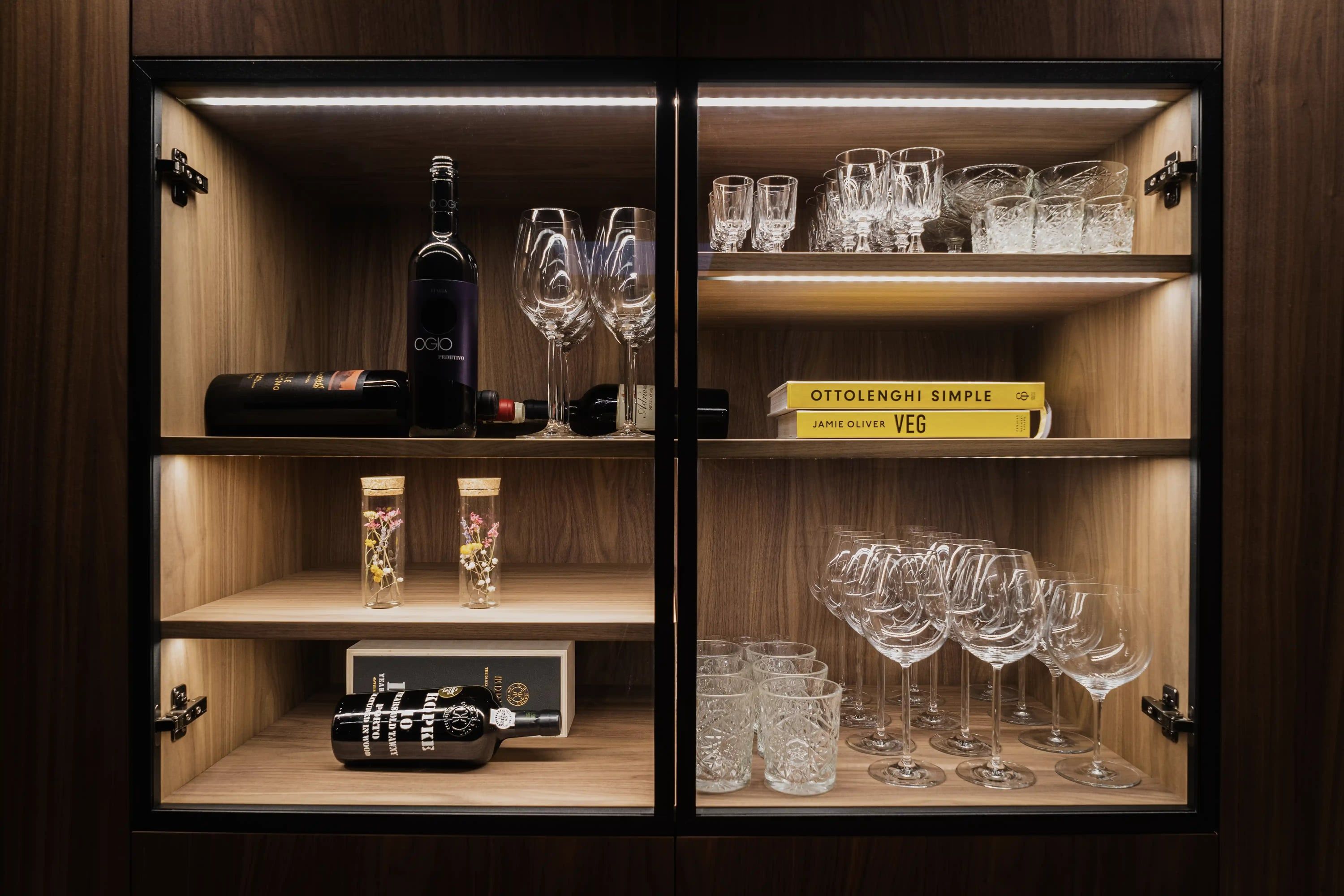Verlichte vitrine met wijnflessen, glazen en kookboeken
