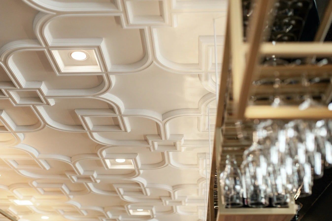 Ornamentplafond met inbouwspots boven de glazen in het barrek