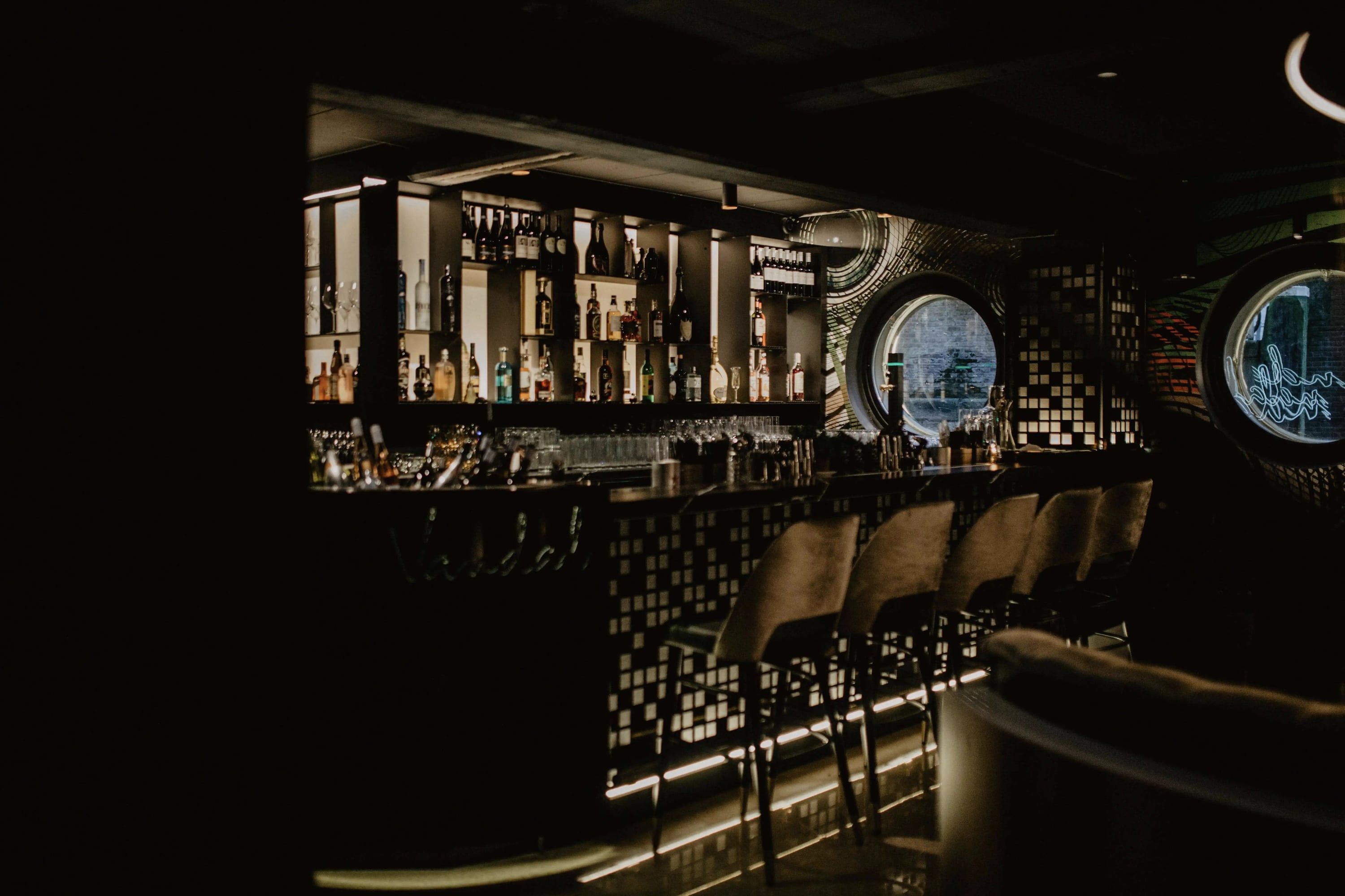 Bar met verlichte flessenwand en barkrukken in het donker