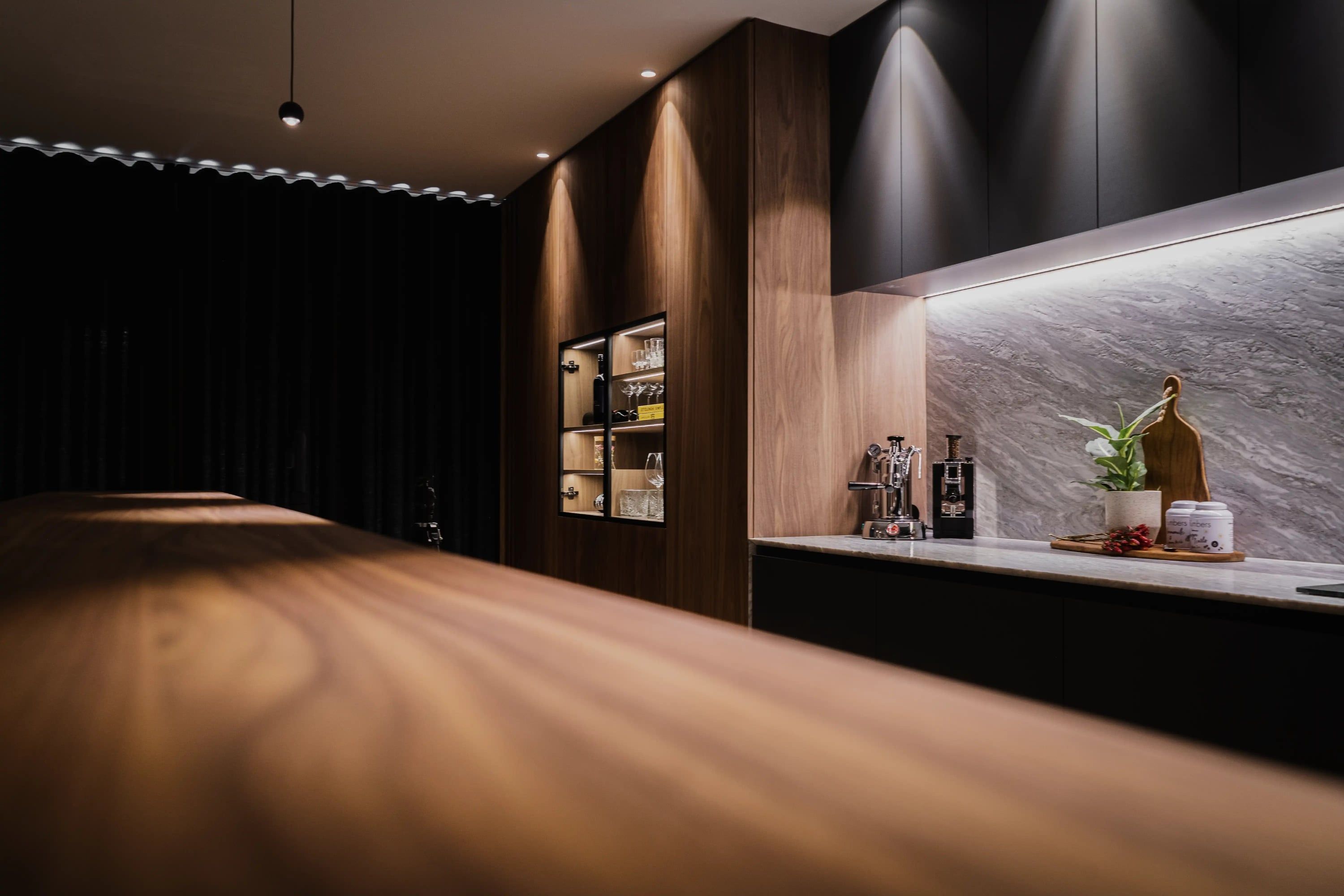 Houten eettafel in strijklicht met de keuken en de verlichte vitrine op de achtergrond