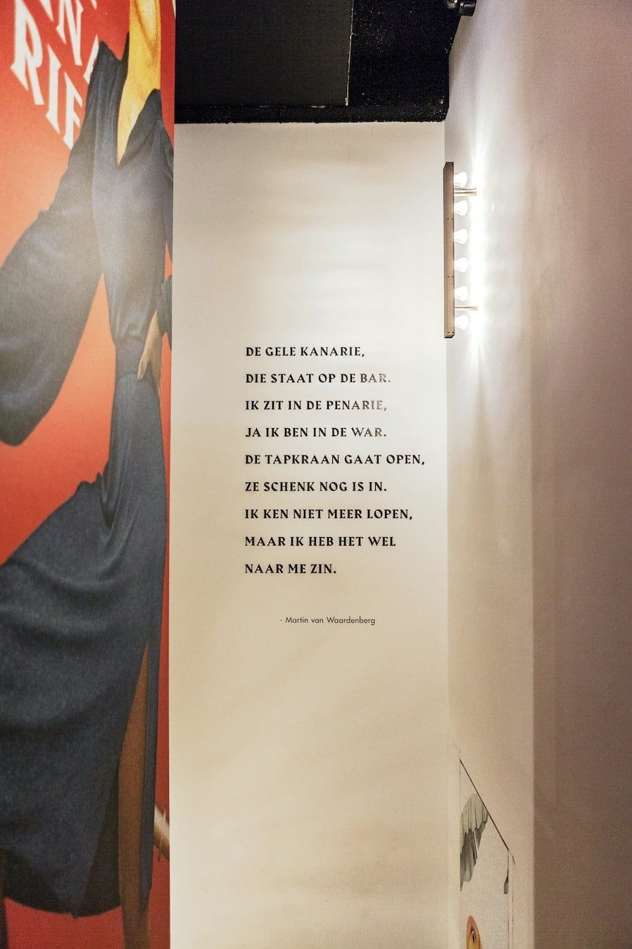 Wand met het gedicht De Gele Kanarie naast een schildering, aangelicht door een verticale wandlamp