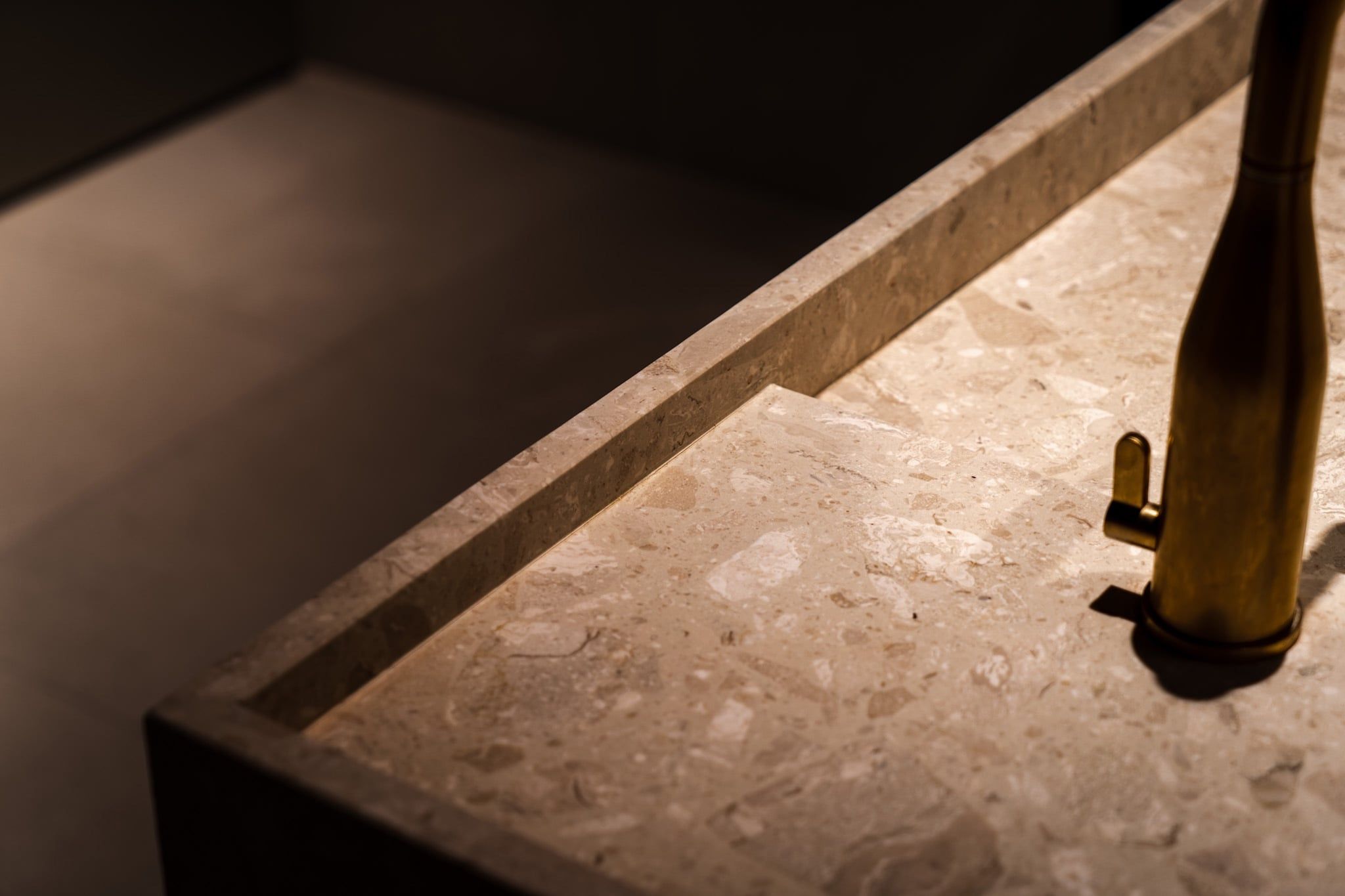 Detail van een terrazzo wastafel met messing kraan in strijklicht