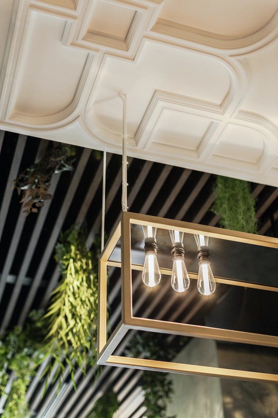 Messing hanglamp met drie gloeilampen onder het ornamentplafond