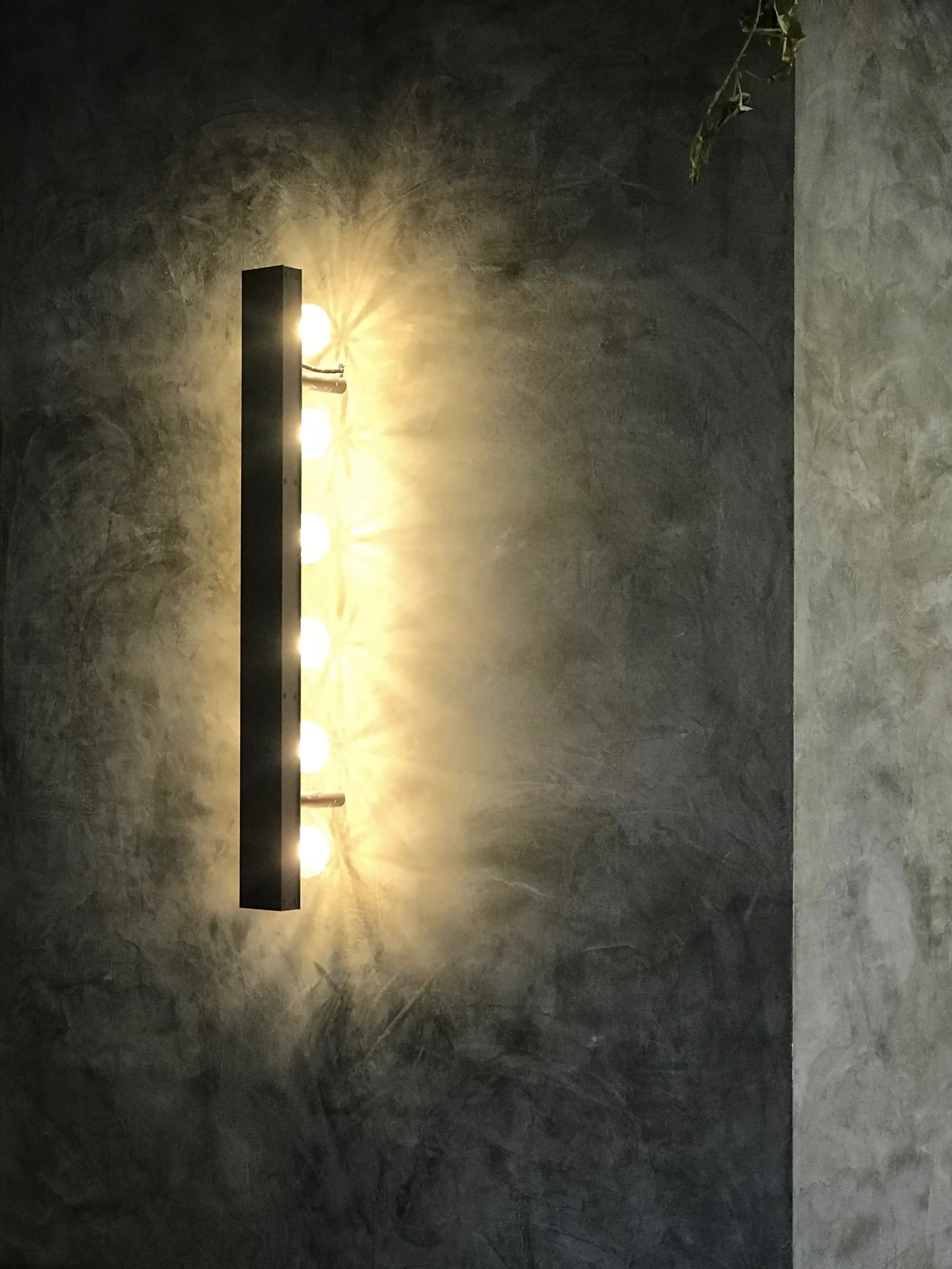 Verticale wandlamp met lichtbollen op een stucwand